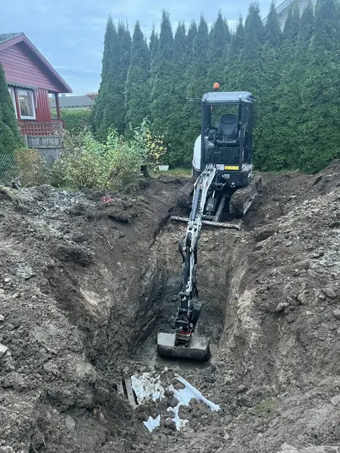 Minigraver i en dyp grøft ved et hus
