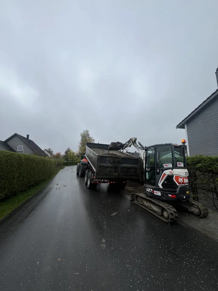 Minigraver laster en lastebil på en våt vei